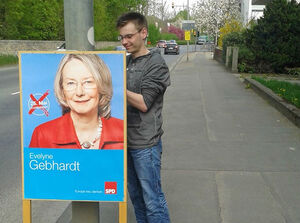 Jonas Köhnert befestigt ein Plakat von Evelyne Gebhardt MdEP